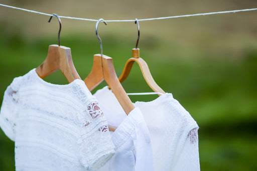 freshly cleaned white clothing on wooden hangers being aired outdoors