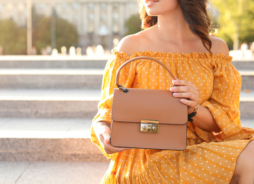 a close up of a stylish woman wearing a yellow polka dot dress and a tan colored handbag