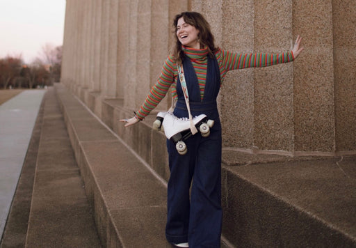Emily in a blue jumpsuit and striped roll neck with carrying roller skates over her shoulder