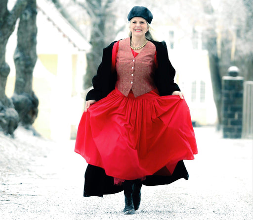 Eva stepping out in the snow in a stunning red dress and black coat and hat