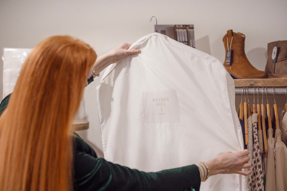 A woman in a clothes shop holding up a Hayden Hill Garment Bag