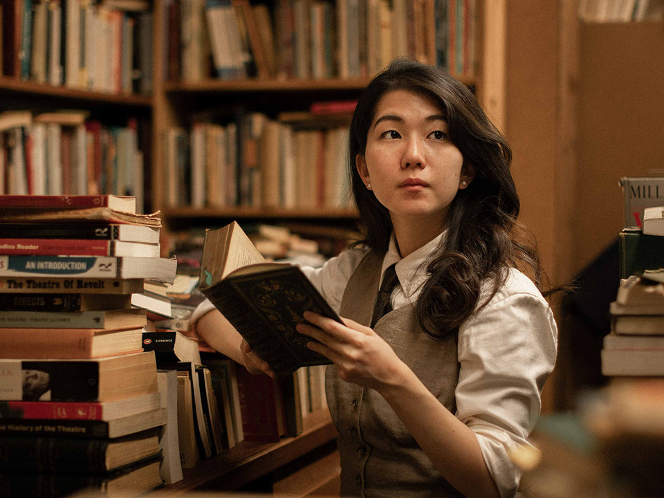 Mai in the library in a shirt, waistcoat and tie