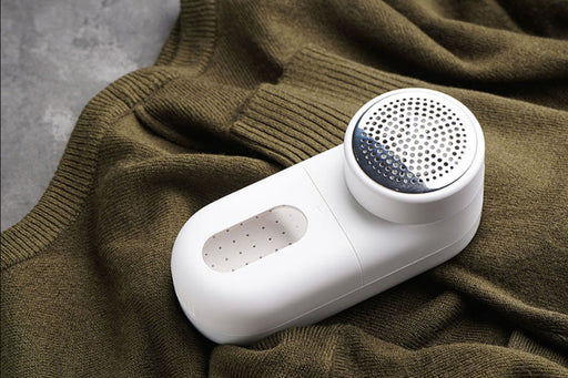 a white fabric shaver lying on an olive green sweater