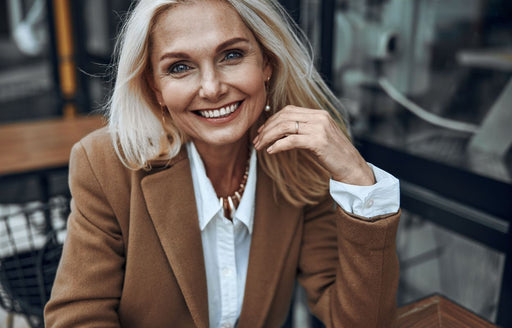 a beautiful blonde older woman wearing a classic white shirt and a camel colored overcoat