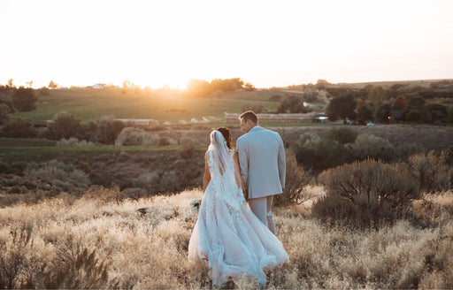 a beautiful romantic shot of Riquel and her husband standing in a field at sunset on their wedding day