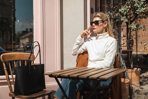 a chic woman in a turtleneck cream sweater and sunglasses enjoying the sunshine at a café