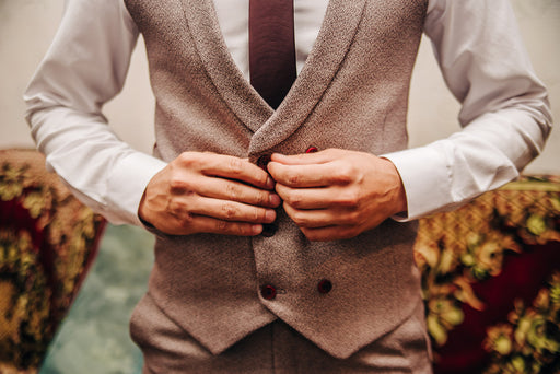 a close up of a man’s hands buttoning his vest