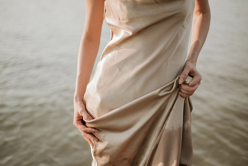 a close up of a woman standing in a lake wearing a silk dress