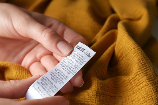 a close up of hands holding a care label on a mustard yellow garment