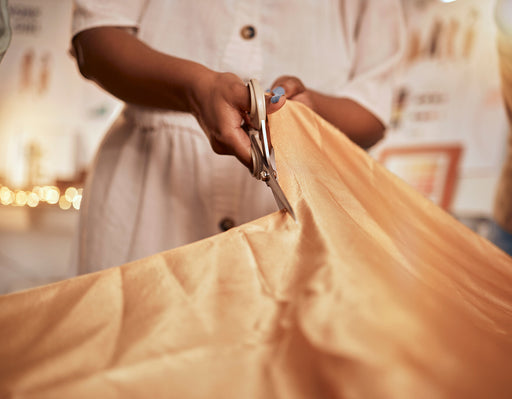 a large piece of golden-colored silk being cut by a tailor