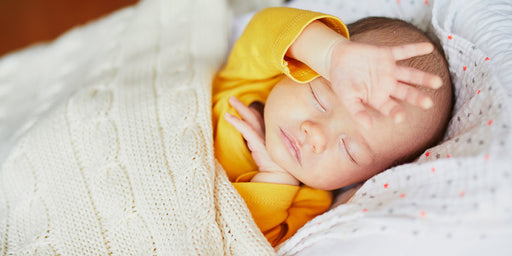 a newborn baby sleeping in a yellow sleeved cotton top under a cable knit blanket