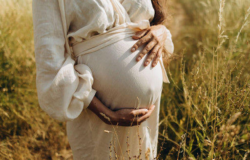a pregnant woman standing in a sunny field