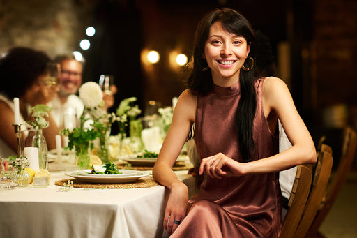 a smiling woman seated in a restaurant wearing a brown silky sleeveless dress