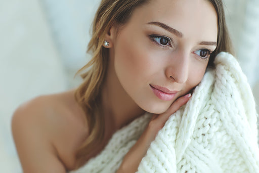 a woman holding a soft cream wool knit next to her cheek
