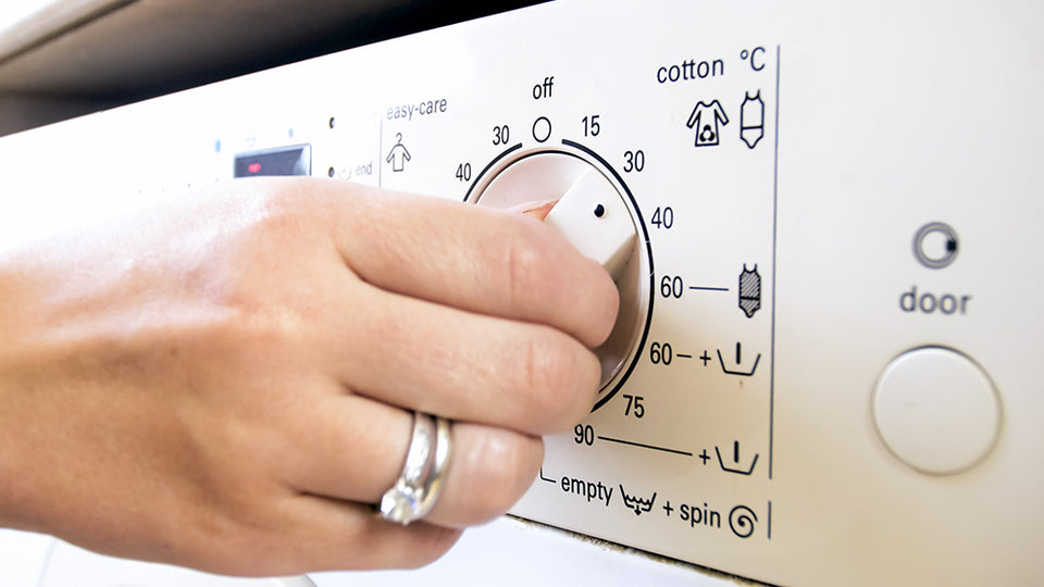 a womans hand adjusting the washing machine temperature to 30℃