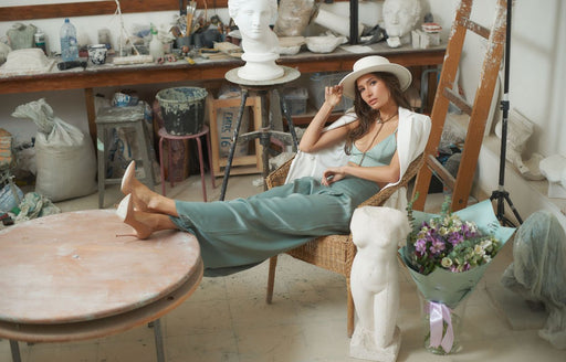 a woman sitting in an artist’s studio wearing pale green palazzo pants with a cream blazer and hat