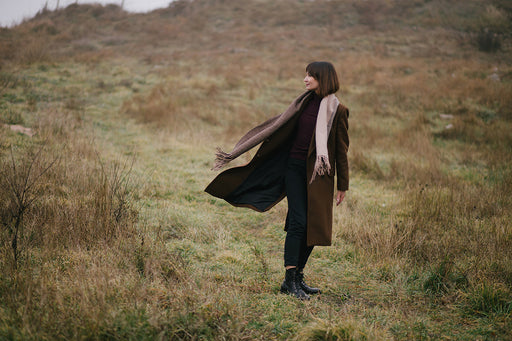 a woman standing in a field wearing a long woolen scarf