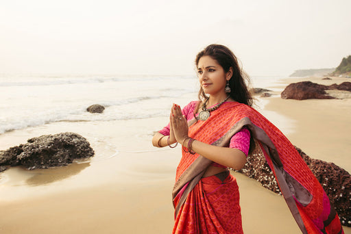 a woman standing on the beach wearing a bright red patterned sari