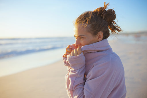 a woman standing on the beach wrapped in a pale pink fleece