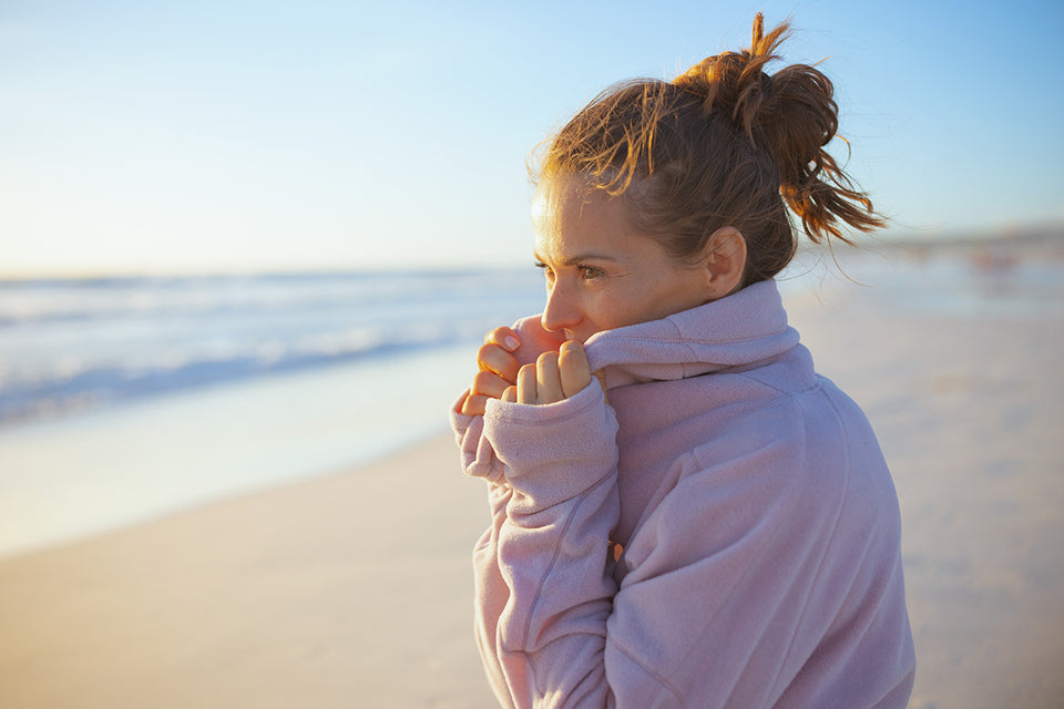 a woman standing on the beach wrapped in a pale pink fleece