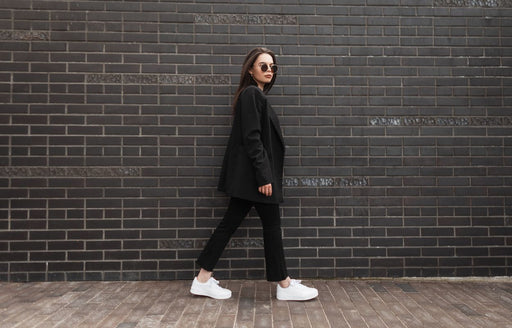a woman wearing a black blazer and pants with white sneakers
