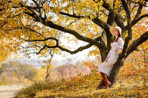 a woman wearing a long white dress and leather boots surrounded by Fall scenery