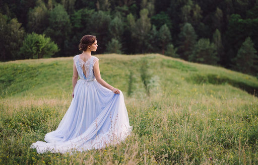 a woman wearing a pastel blue gown standing in a field