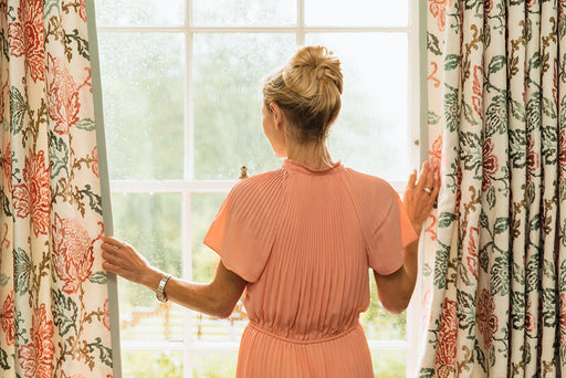 a woman wearing a peach colored pleated dress looking out of the window