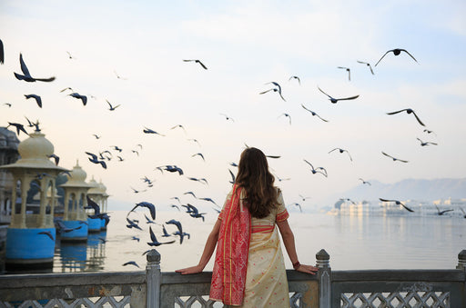 a woman wearing a sari standing on a bridge by the water