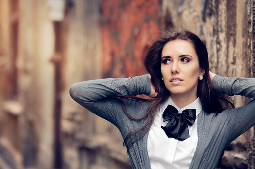 a woman wearing a white shirt black bow tie with a gray cardigan