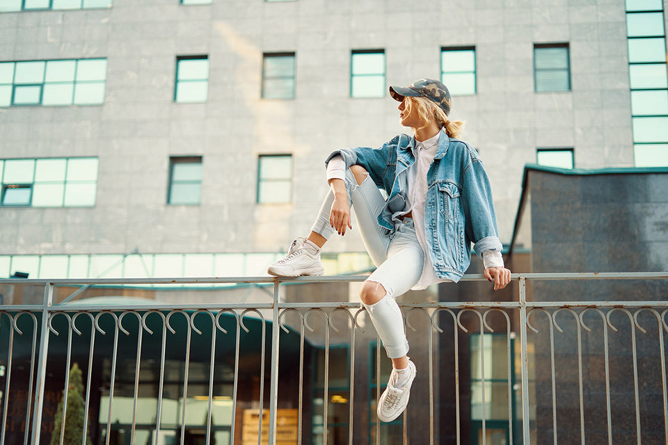 a woman wearing hip-hop style ripped jeans, sneakers, oversized denim jacket and baseball cap