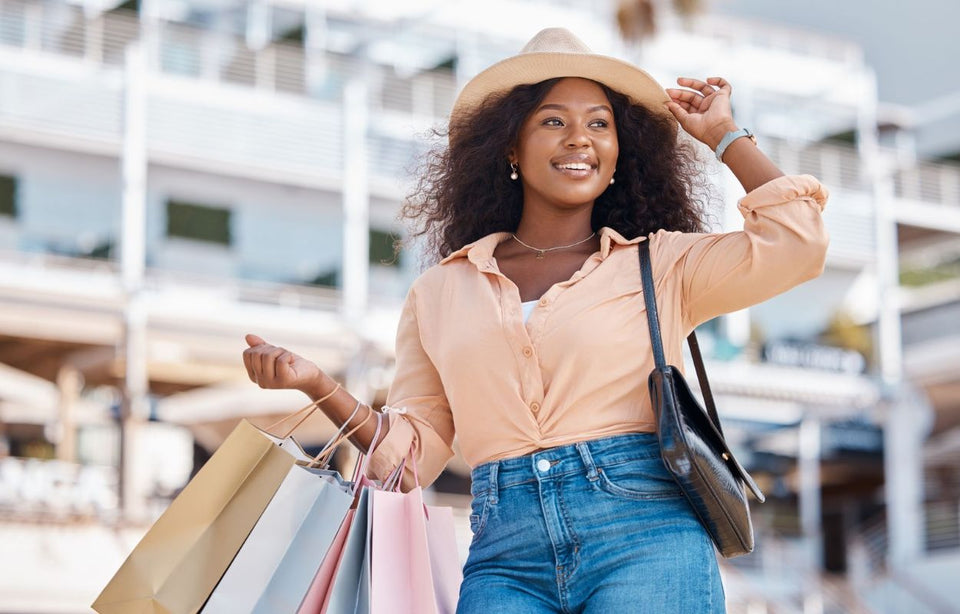 a woman wearing jeans an apricot color shirt and a straw hat carrying several shopping bags