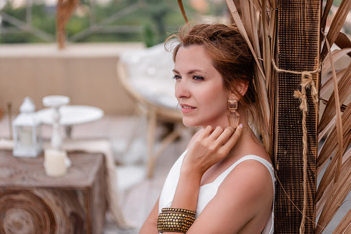 a woman wearing statement jewelry consisting of chunky earrings and a large brass bangle