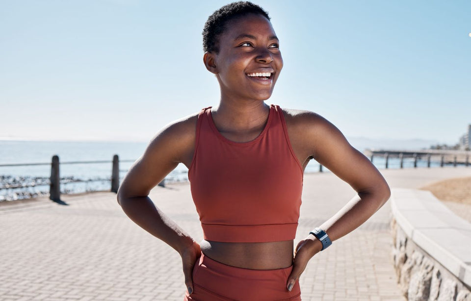 a woman with an athletic build in a rust top and shorts, who has just ended her run on a coastal sidewalk