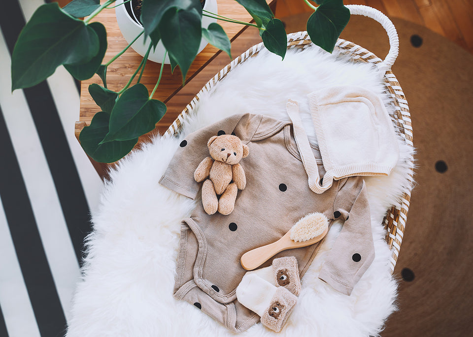 a woven basket containing a newborn baby’s bodysuit and accessories