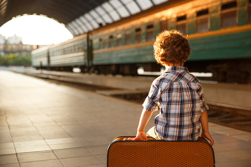 a young child sitting on a suitcase at the train station
