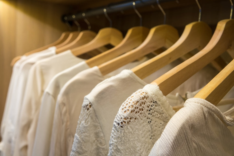 a row of white shirts and white lace tops on wooden hangers