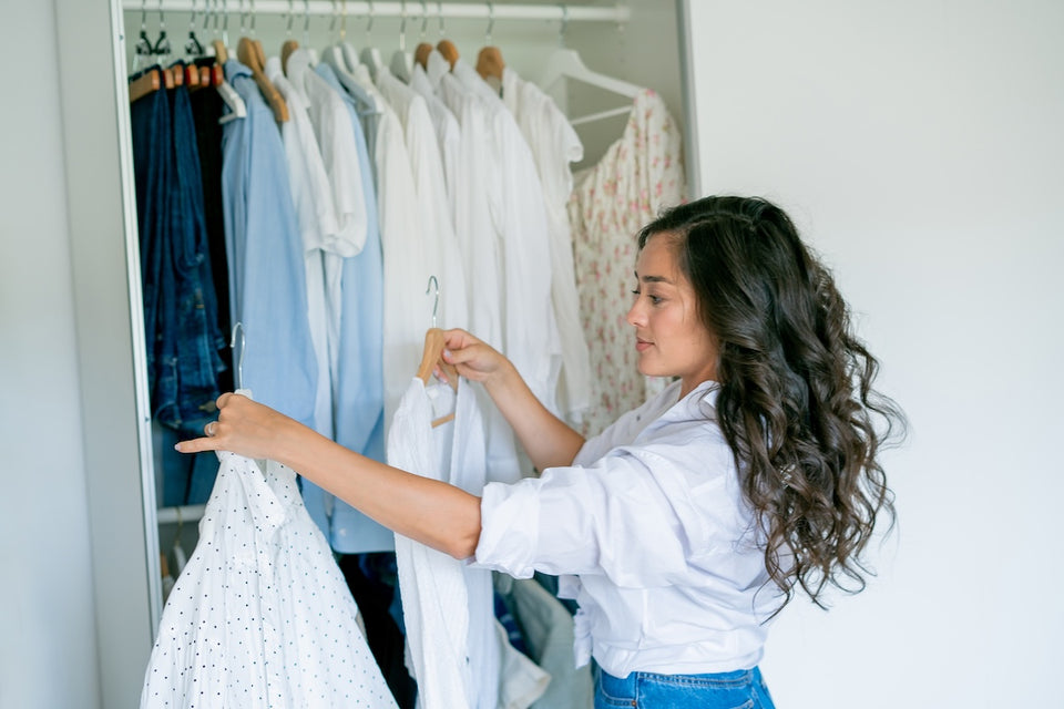 a woman standing in front of her closet looking at her summer shirts on hangers
