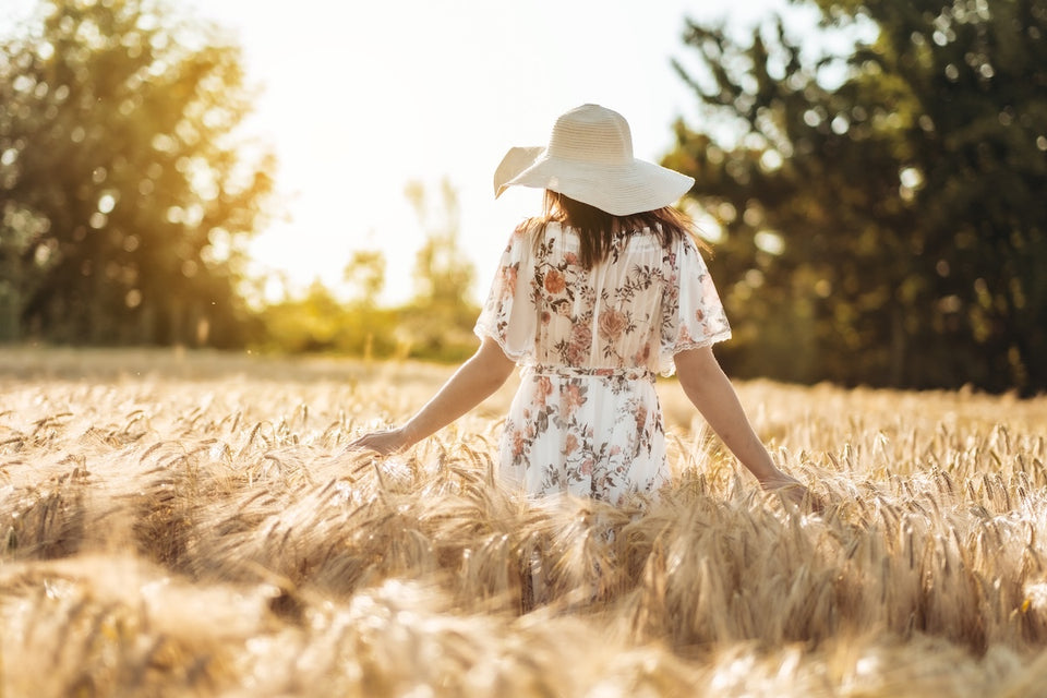 a woman in a pretty floral print summer dress and a straw hat walking through a corn field