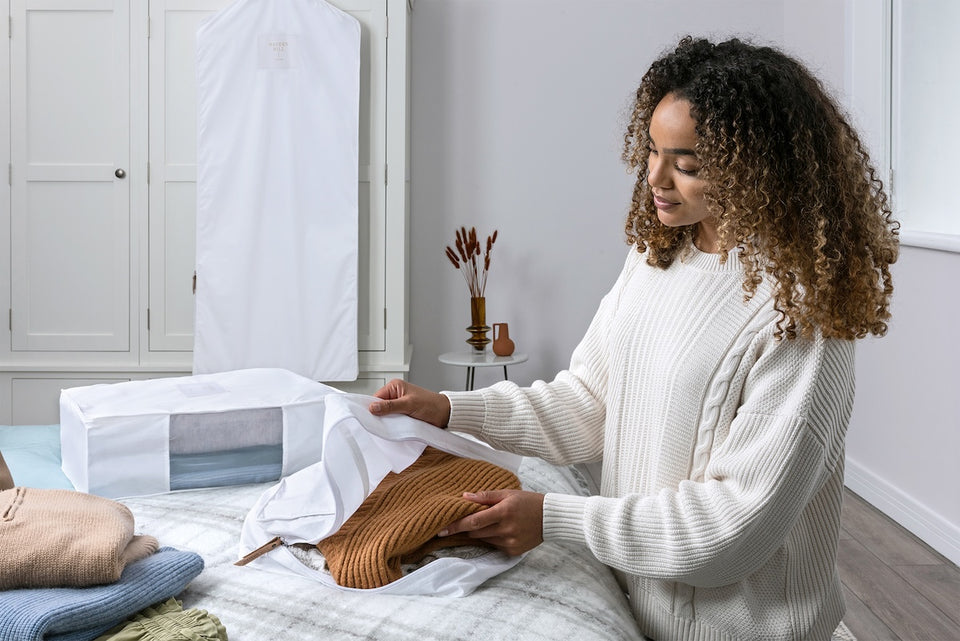 a woman placing a brown knit sweater into a large storage bag