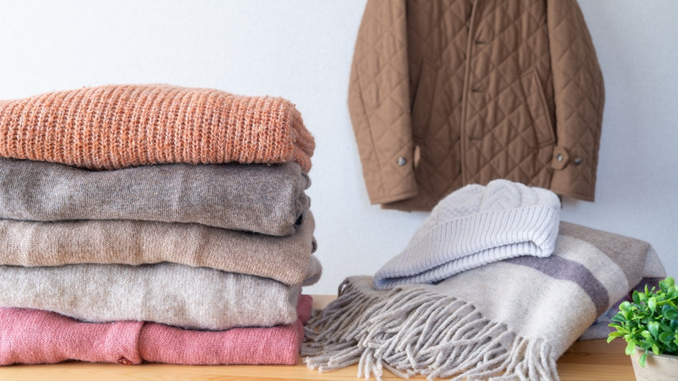 a pile of folded soft sweaters next to a scarf and wool hat