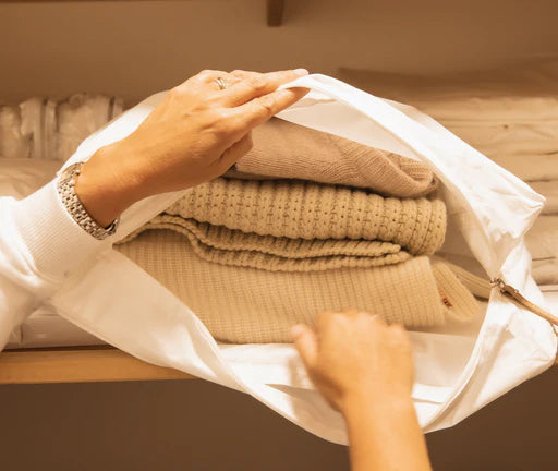 opening a Hayden Hill organic cotton garment storage bag that is filled with sweaters