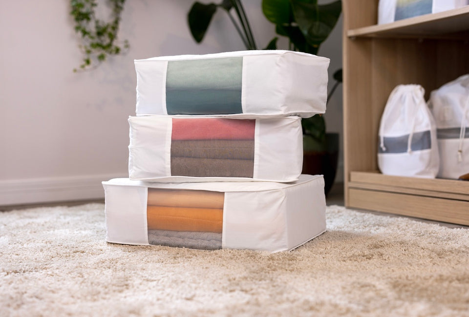 a stack of three white Hayden Hill Storage bags with colorful sweaters stored inside