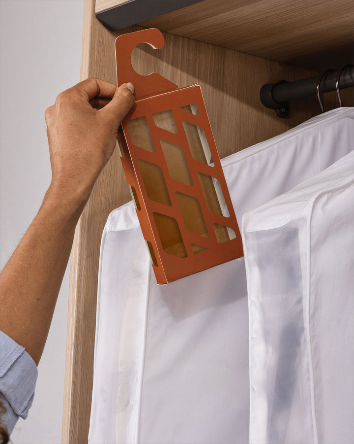 a moth trap being hung in a wardrobe next to clothing in storage bags