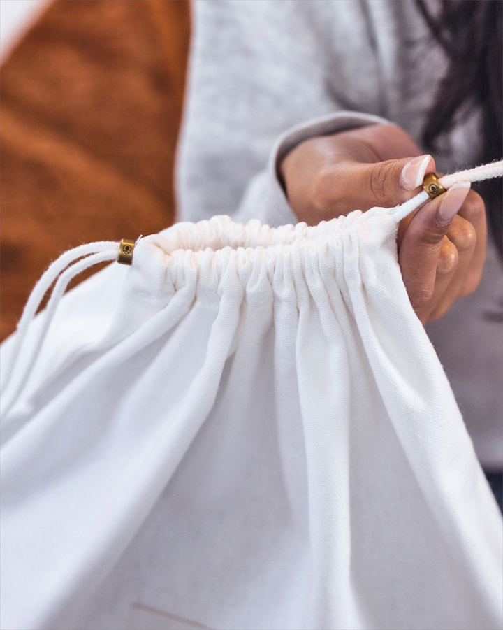a close up of the drawstring detail on a dust bag with one of the brass sliders being held in a woman's hand