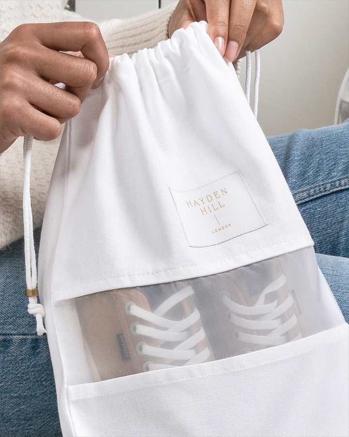 hands holding the top of a dust bag with a pair of sneakers visible through the organza panel