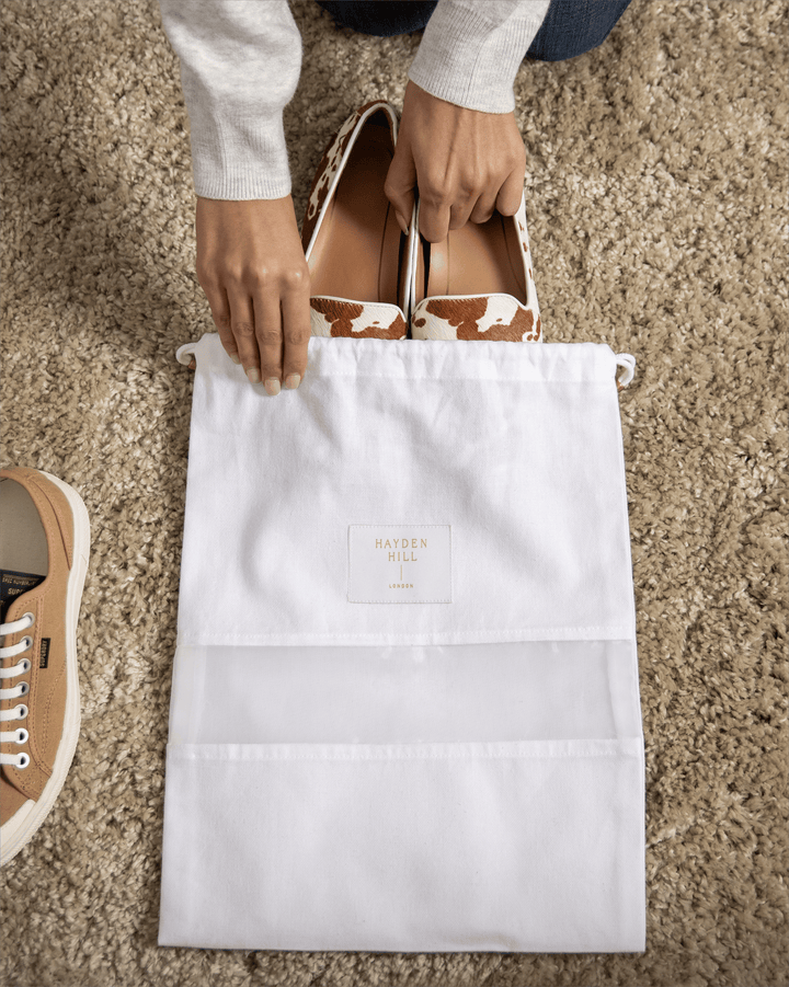a top view of a dust bag lying on a rug with pony skin flat shoes being put inside