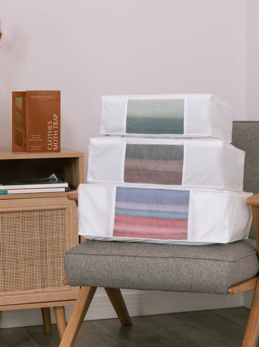 a side profile view of the large, extra large and double extra large storage bag stacked on a chair with a moth trap next to them on a side tabvle