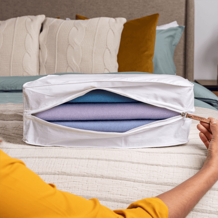 a large storage bag sitting on a bed being unzipped with a view of several woollen sweaters inside