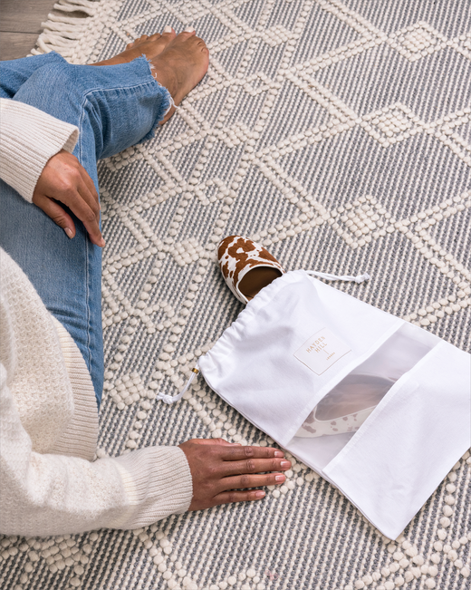 the side of a woman sitting next to a dust bag lying on the floor with pony skin pumps being stored inside